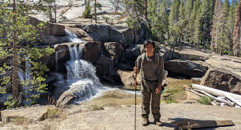 a student poses beside a waterfall on a high sierra backpacking course for bipoc